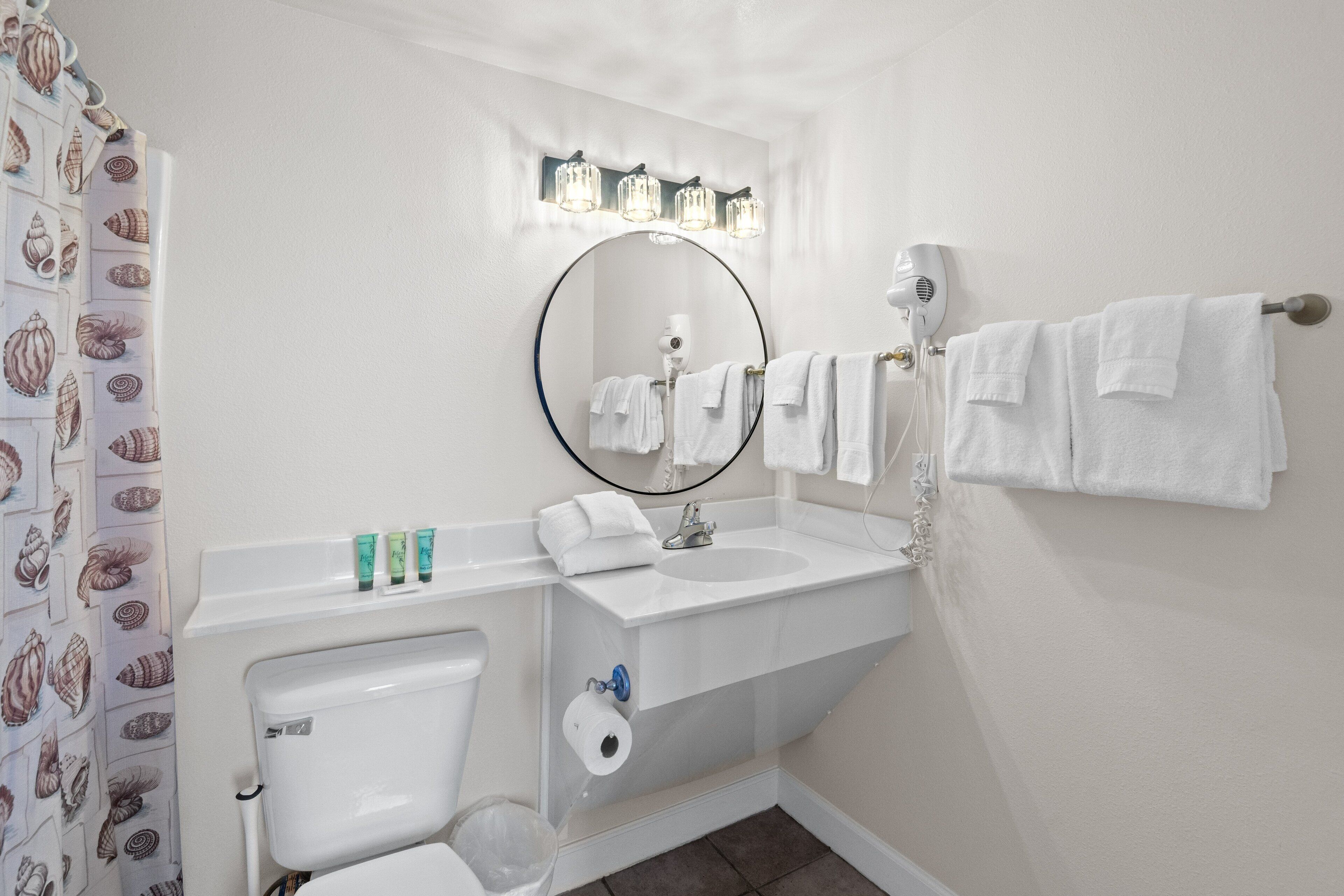 A bathroom with a toilet, sink, and mirror. There are towels hanging on a rack, and a shower curtain with a shell pattern.