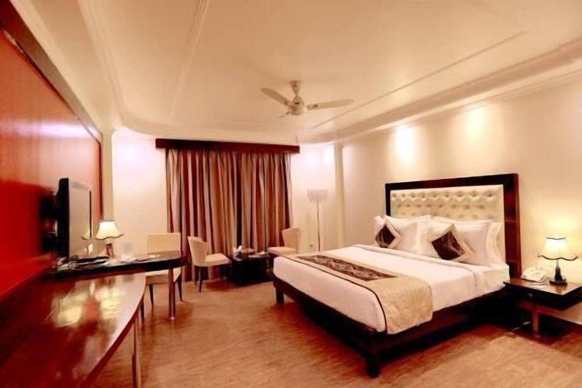 A hotel room with a bed, bedside tables, a desk, a chair, a ceiling fan, and a window with curtains.