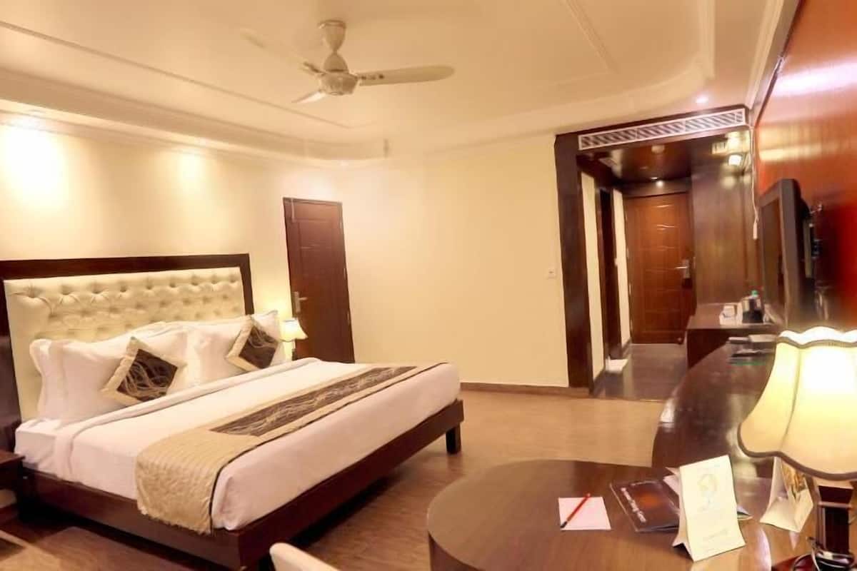 A hotel room with a bed, bedside table, lamp, and a desk with papers.
