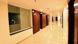 Un long couloir bien éclairé, avec des portes en bois et un mur en verre d’un côté.