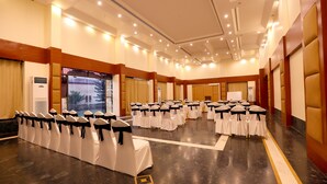 Une grande salle de conférence avec de longues rangées de chaises blanches, des écharpes noires et des tables disposées pour une réunion.