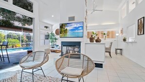 Un espacio habitable amplio con un televisor grande, sillas de mimbre, una chimenea y vistas al exterior.