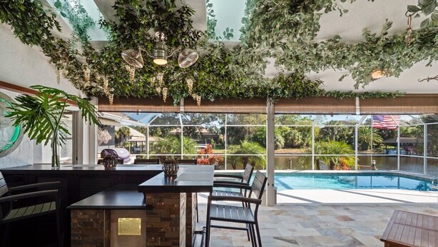 Un área de piscina interior con bar y asientos, rodeada de grandes ventanales y vegetación.