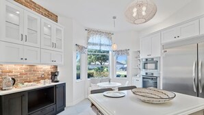 Una cocina moderna con armarios blancos, una pared de ladrillo decorativa, una isla grande y vistas al exterior.