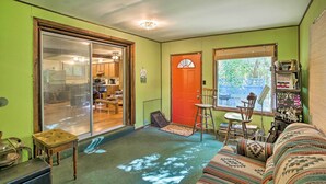 A cozy living room with a green wall, a sliding glass door leading to a kitchen, a red door, and a window with blinds. - Rustic Cottage with Fire Pit & Private Yard! (Fenwick)