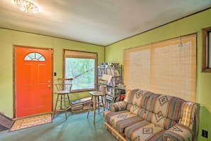A cozy living room with a patterned sofa, a wooden chair, a bookshelf, and a red door.