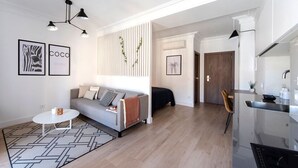 Un salon moderne avec un canapé, une table basse et un tapis à motifs. On y trouve également un coin cuisine équipé d’une cuisinière et d’une table à manger.
