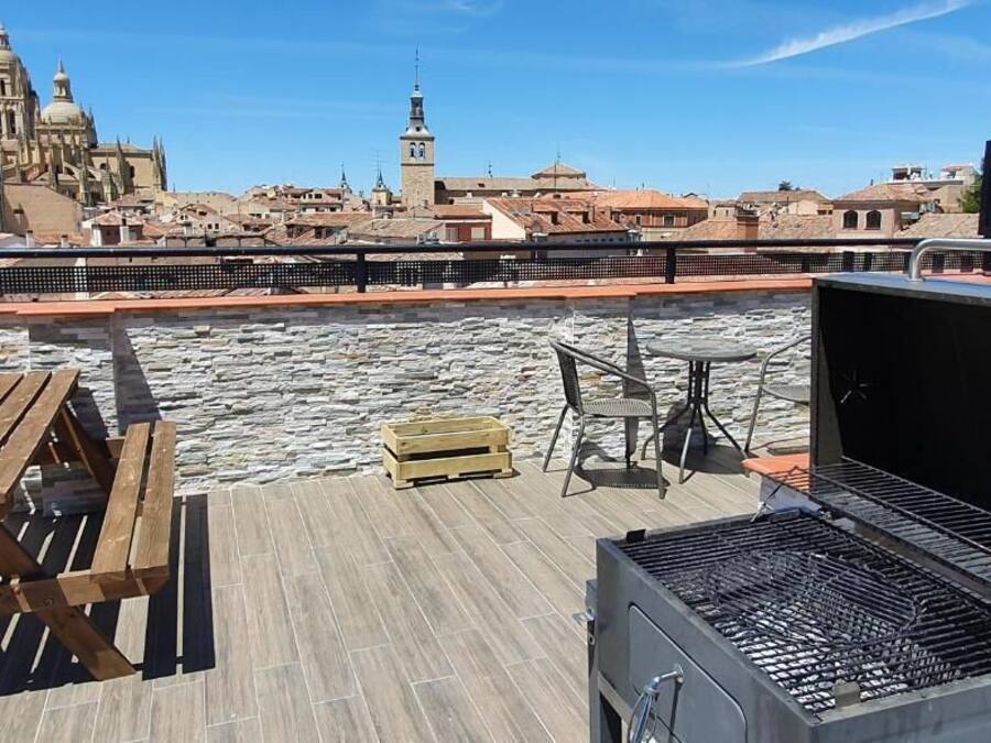 Una terraza en la azotea con una parrilla, mesas de madera y vistas a edificios históricos.