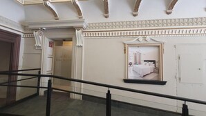 Un couloir d’hôtel avec un escalier, un tableau encadré au mur et une porte avec une pancarte.