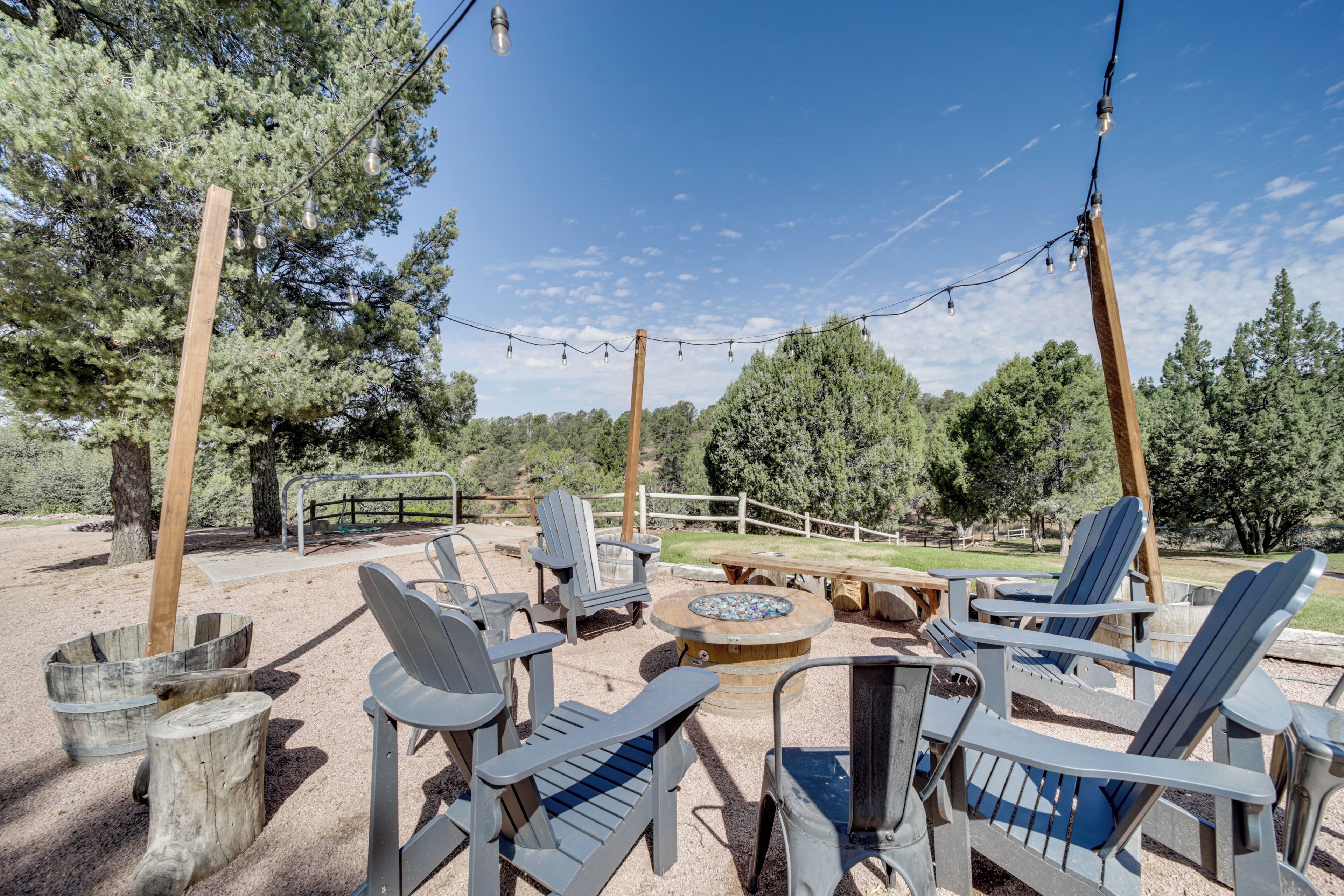 Un espace extérieur aménagé avec des chaises Adirondack et un foyer, entouré d’arbres et d’une clôture en bois.