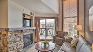 A living room with a stone fireplace, a sofa, a coffee table, and a television. - Ski-In/Out Condo in Snowshoe Mountain Resort! (Snowshoe)