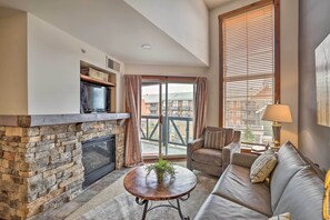 A living room with a stone fireplace, a sofa, a coffee table, and a television. - Ski-In/Out Condo in Snowshoe Mountain Resort! (Snowshoe)