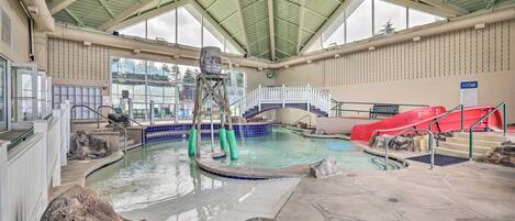 An indoor swimming pool with a water slide, a lifeguard tower, and a covered roof structure.