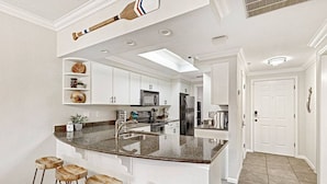 A modern kitchen with white cabinetry, granite countertops, and a central island with stools. - `Lakeside Haven`- Hot Tub, Pool, Lake view! (Lago Vista)