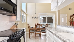 A kitchen with a black stove, white cabinets, a dining table with chairs, and a chandelier.