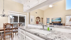 A kitchen with a granite countertop, white cabinets, a built-in dishwasher, a dining area with a wooden table and chairs, and a ceiling fan.