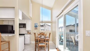 A kitchen with white cabinets, a dining table with chairs, a chandelier, and a view of a balcony with outdoor seating.
