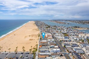 Vue aérienne d’une ville côtière avec une longue plage de sable, une marina remplie de bateaux et un quartier résidentiel densément peuplé, avec ses rues et ses immeubles.