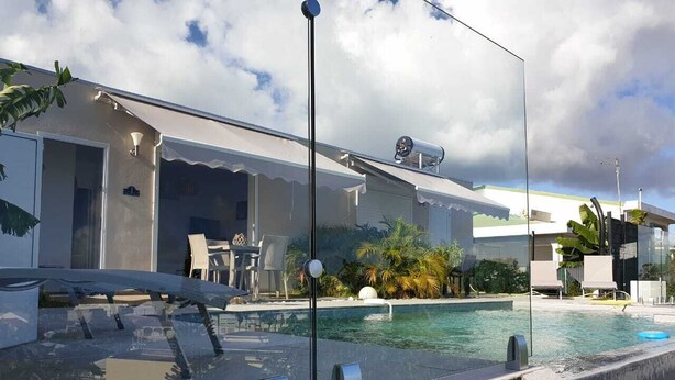 Zona de piscina moderna amb aigua cristal·lina, gandules i una tanca de vidre.