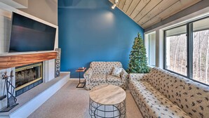 A cozy living room with a fireplace, a large flat-screen TV, a wooden ceiling, and a Christmas tree. - Lincoln Retreat w/ Village of Loon Amenity Access (Lincoln)