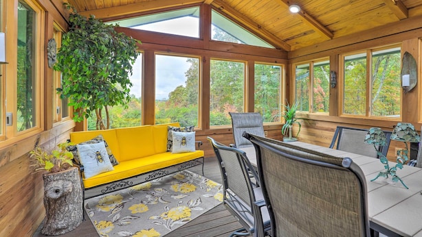Un interno in legno con un divano giallo, un tavolo da pranzo e sedie, ampie finestre e una ventola a soffitto.