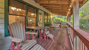 Un portico riparato con poltrone Adirondack e un tavolo, travi in legno e ampie finestre che si affacciano su una foresta.