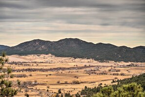 A panoramic view of a rural landscape with rolling hills, sparse vegetation, and scattered buildings.