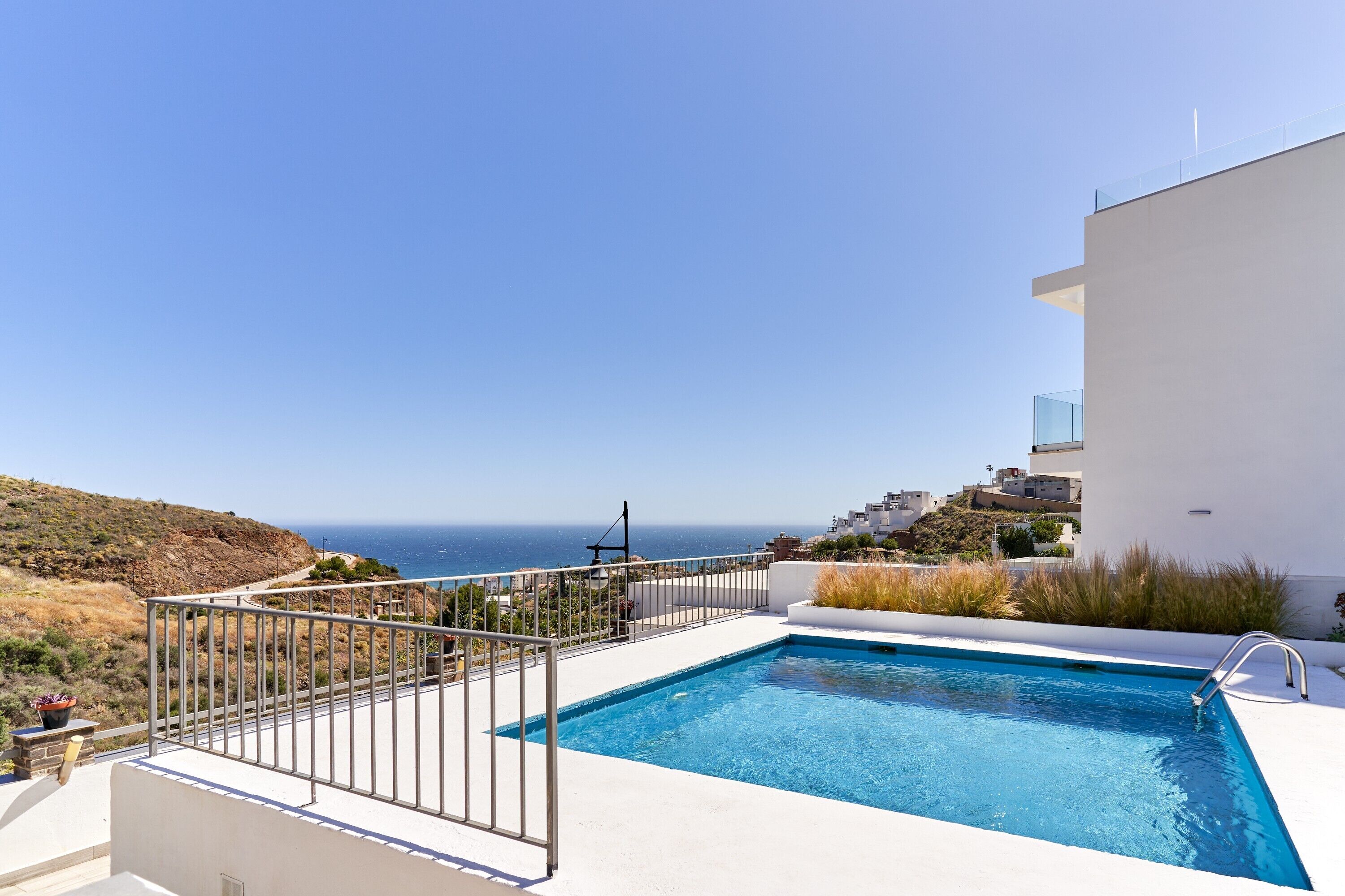 A swimming pool with a view of the sea, a white building, and a metal railing.