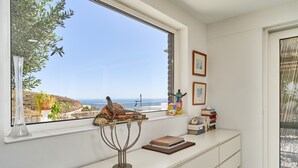 A room with a large window overlooking a coastal view, a white console table with decorative items, and a clear sky. - Villa Spectacular Casa Negra with Sea View, Pool, Garden & Wi-Fi (Torrox Costa)