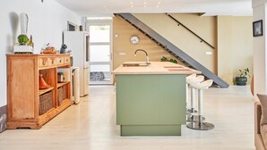 A modern kitchen with a green island, wooden cabinets, and a staircase leading to another level. - Villa Spectacular Casa Negra with Sea View, Pool, Garden & Wi-Fi (Torrox Costa)