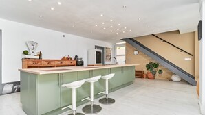 A modern kitchen with a central island, bar stools, a refrigerator, and a staircase. - Villa Spectacular Casa Negra with Sea View, Pool, Garden & Wi-Fi (Torrox Costa)