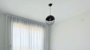Un dormitorio con cama, almohadas, una mesita de noche con lámpara y una ventana con cortinas.