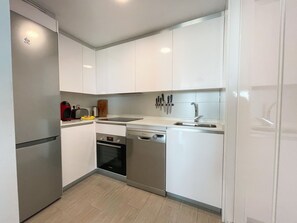 A modern kitchen with white cabinets, a stainless steel refrigerator, a dishwasher, and a sink.