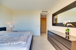 Une chambre à coucher comprenant un lit, une lampe de chevet, une commode, un miroir et un pot d’orchidée.