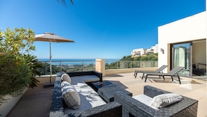 Una terrazza sul tetto con posti a sedere all'aperto, vista sul mare e un edificio moderno sullo sfondo.