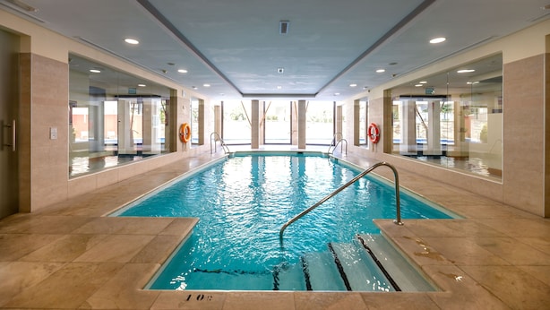 Una piscina interna con acqua cristallina, circondata da pareti di vetro e pavimento piastrellato.