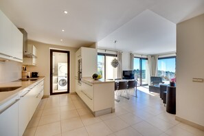 A modern kitchen with a built-in washing machine, a dining area with a TV, and a balcony with a city view.