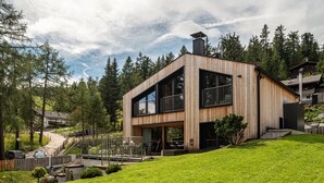 A modern two-story wooden house with large windows, a visible staircase, and a well-maintained lawn.