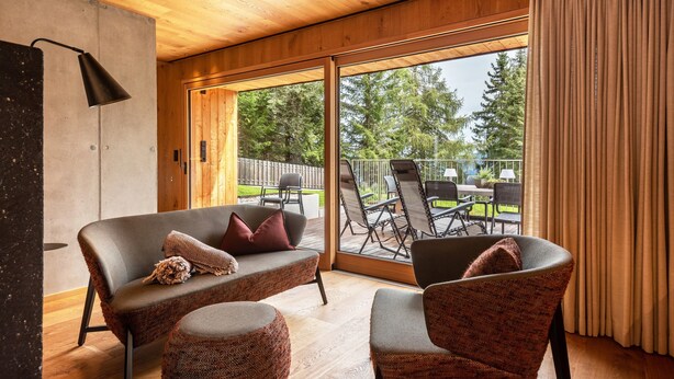 A modern interior with a sofa, armchair, and a large sliding glass door leading to an outdoor patio.