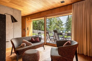 Un interior moderno con sofá, sillón y un gran ventanal corredero que da a un patio exterior.