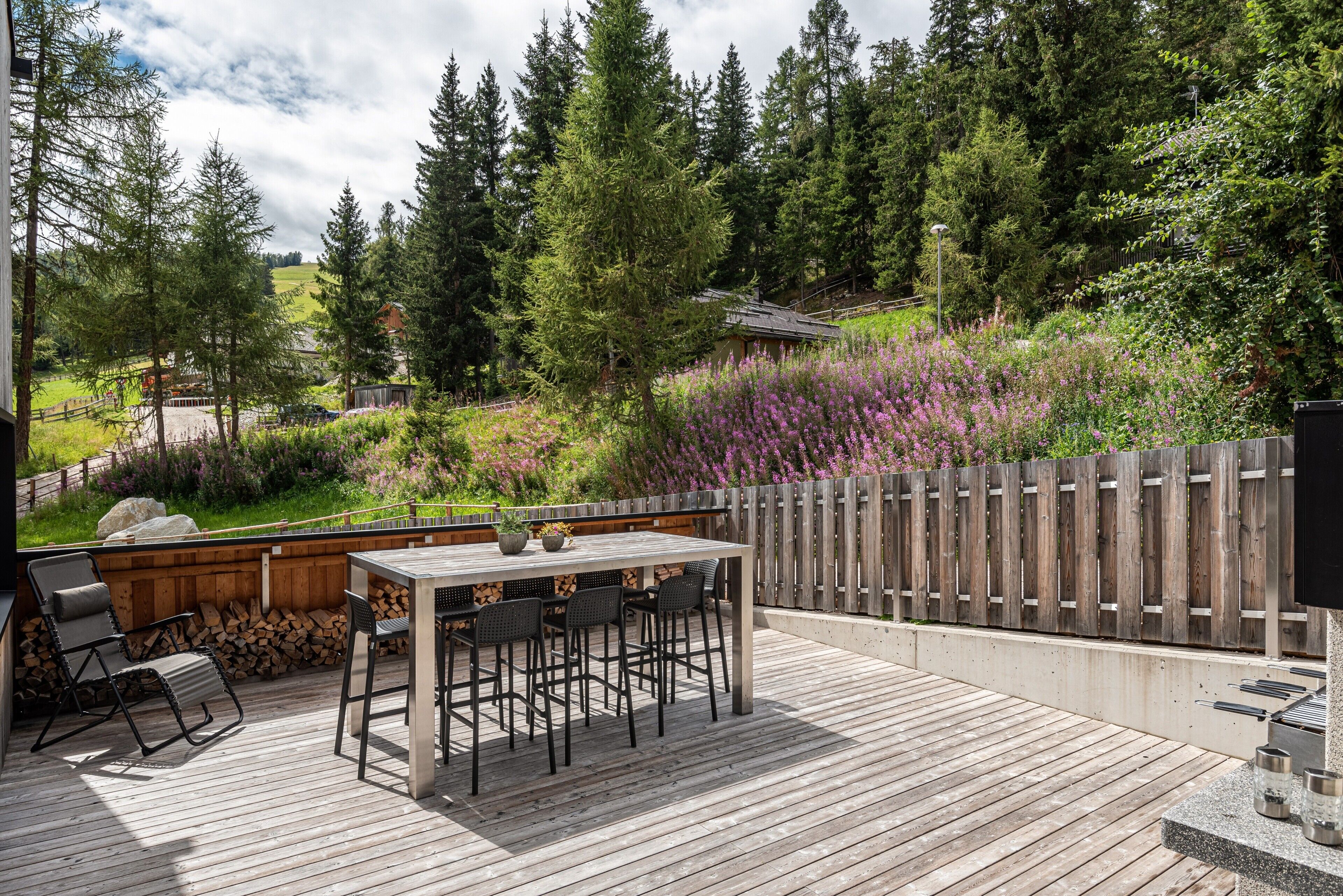 An outdoor deck with a table and chairs, surrounded by a wooden fence and dense greenery.