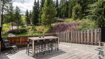 An outdoor deck with a table and chairs, surrounded by a wooden fence and dense greenery.