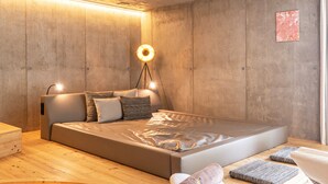 A modern bedroom with a wooden floor, a bed with a headboard, a bedside lamp, and a small artwork on the wall.
