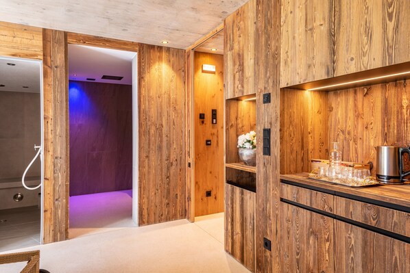 Un baño moderno con paneles de madera, zona de ducha y encimera con hervidor y vasos.