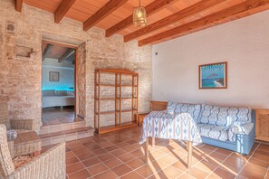A room with a stone wall, wooden beams, a patterned sofa, wicker furniture, and a framed picture on the wall.