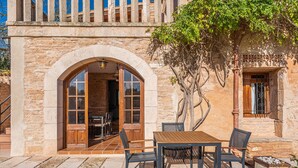 Un bâtiment en pierre avec une porte en arc de cercle, une table en bois avec des chaises, et un arbre devant.