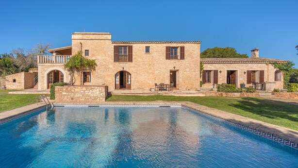 Un edificio de piedra con piscina, arcos y un balcón.