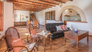 Un salón amplio con techo de madera, un sofá de cuero negro, una mesa de comedor con sillas y una cocina visible a través de un arco.