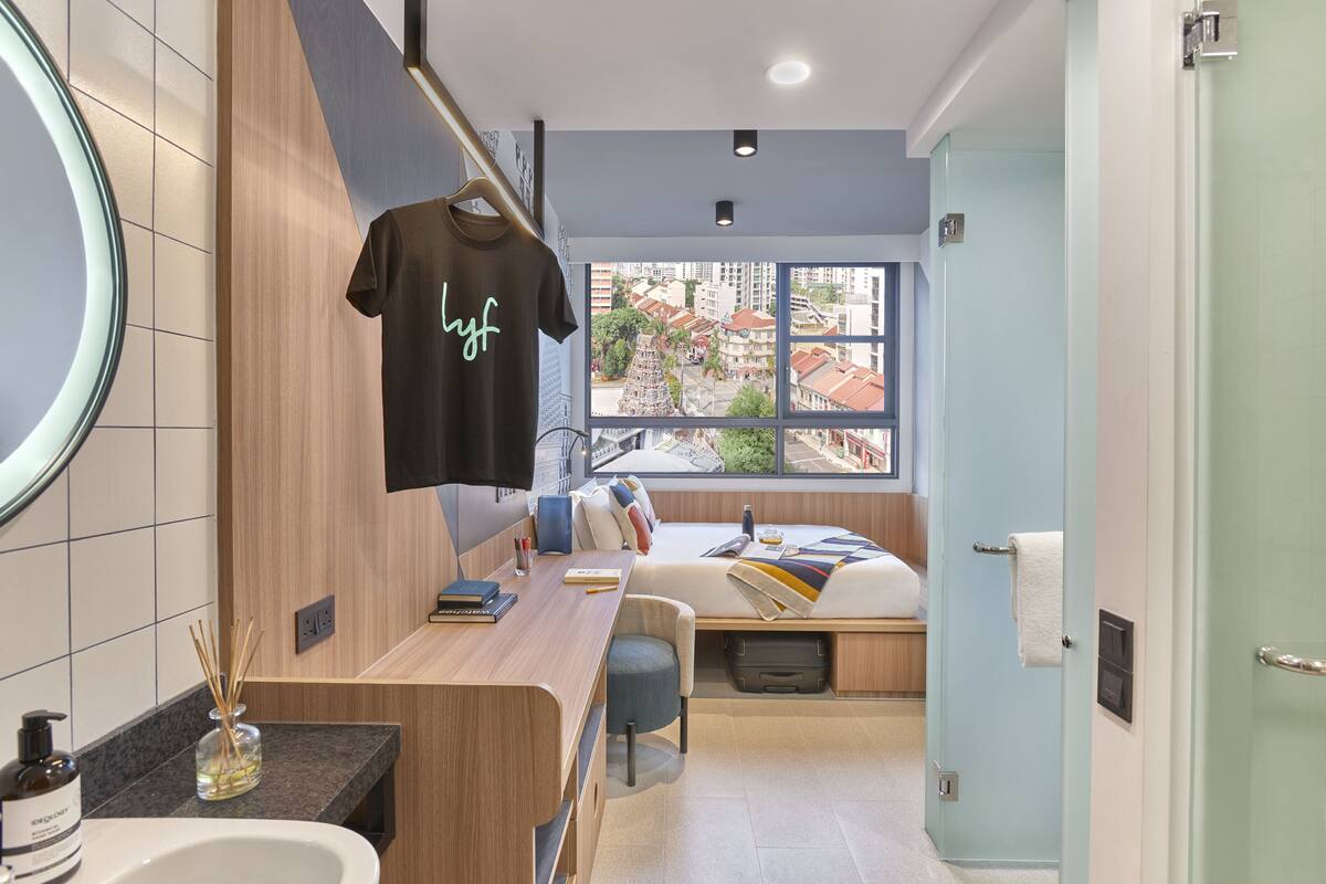 A modern hotel room with a bed, a desk, and a large window offering a city view.