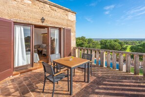 Un balcon avec une table et des chaises en bois, une vue sur la campagne et un bâtiment en pierre avec des volets.